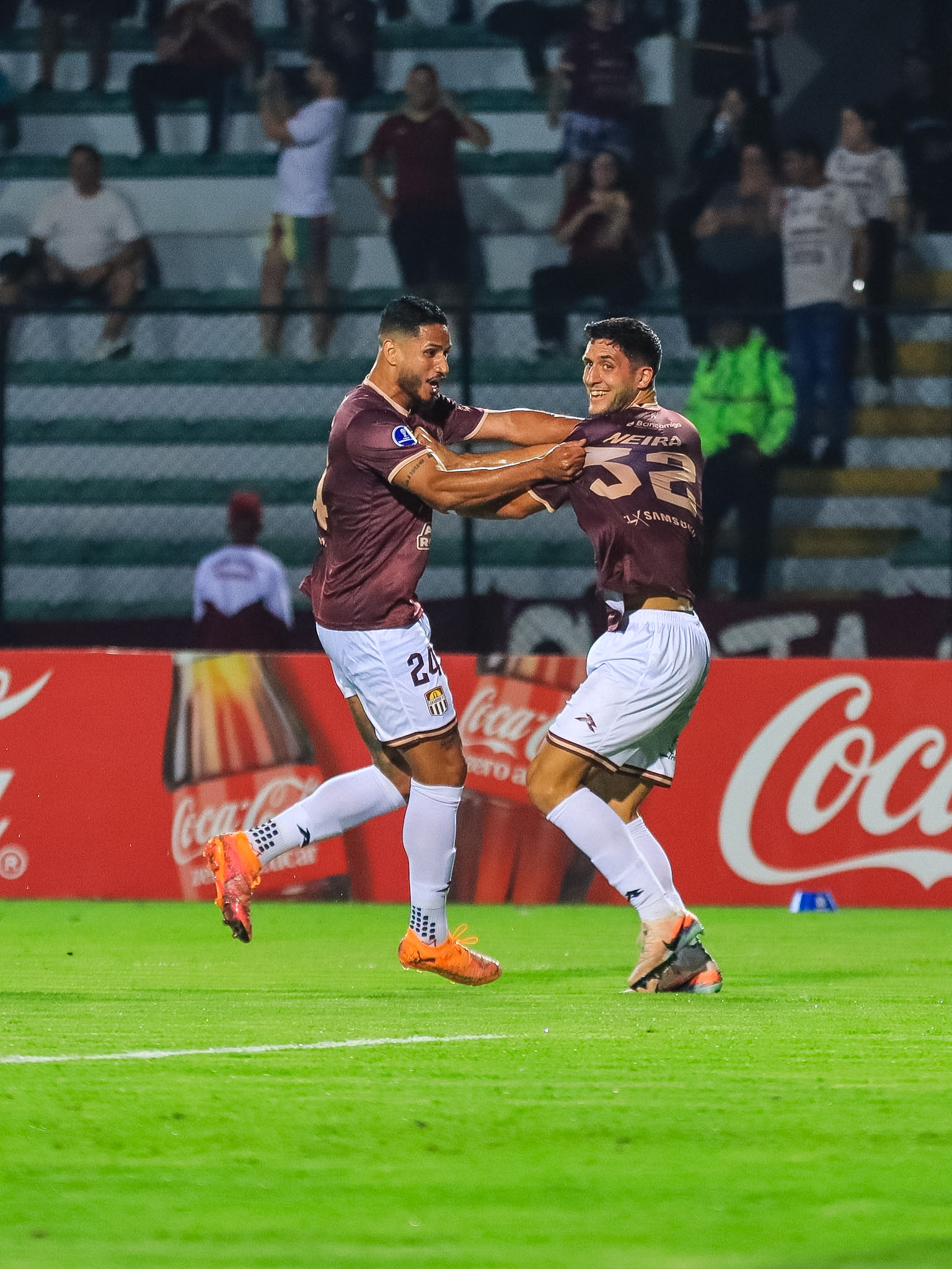 Ezequiel Neira celebra un gol corriendo junto a un compañero, con la tribuna de fondo.